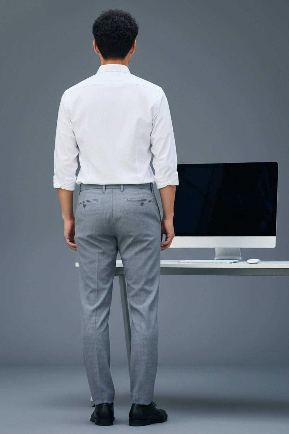 Man in a white shirt and gray pants standing in front of a computer monitor on a gray background