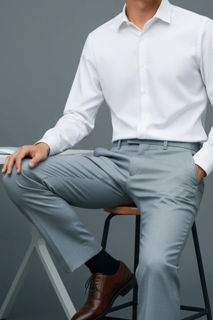 Person wearing a white dress shirt and light gray pants sitting on a stool against a gray background