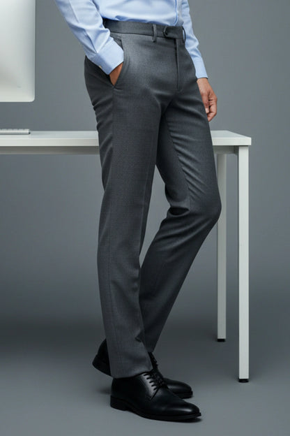 Person wearing gray dress pants with a white shirt and black shoes on a plain background