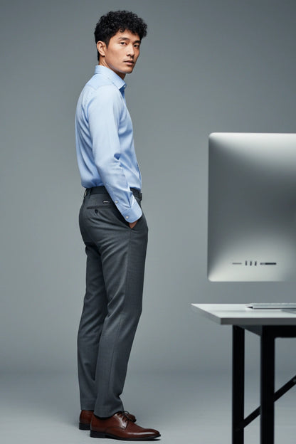 Man in a light blue shirt and gray pants standing next to a computer monitor on a gray background