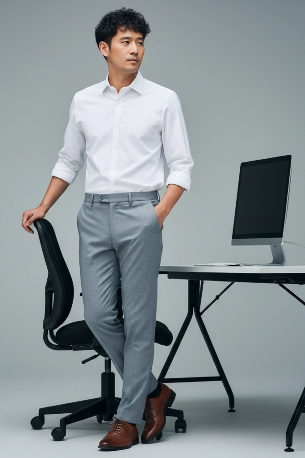 Man in a white shirt and gray pants standing in an office setting with a computer desk.