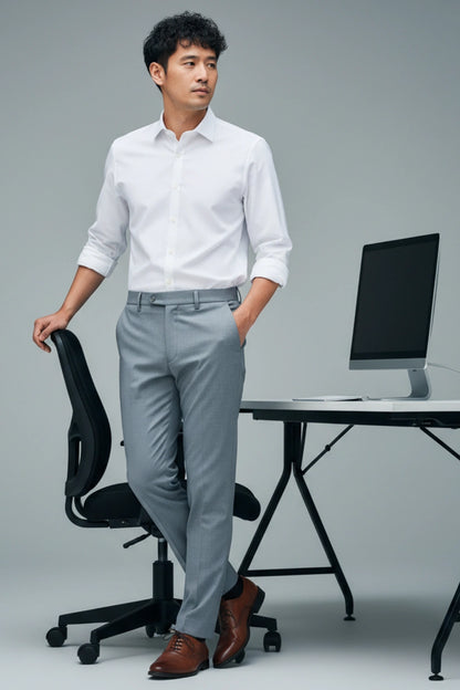 Man in a white shirt and gray pants standing in an office setting with a computer desk.