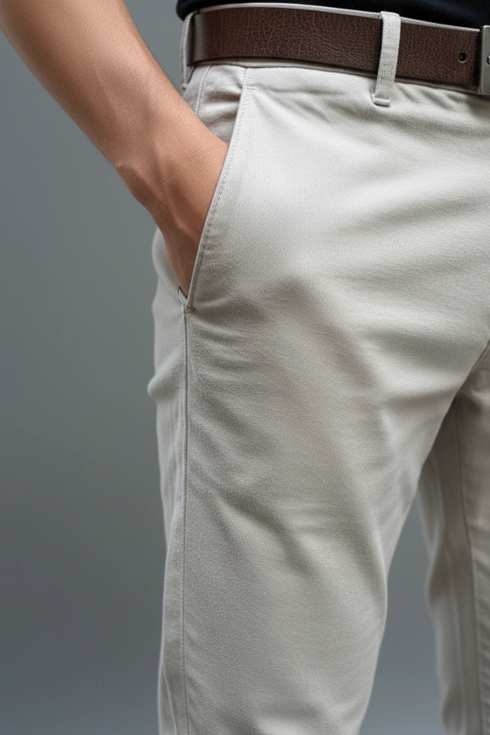 Close-up of light grey cotton pants with a brown belt on a gray background 