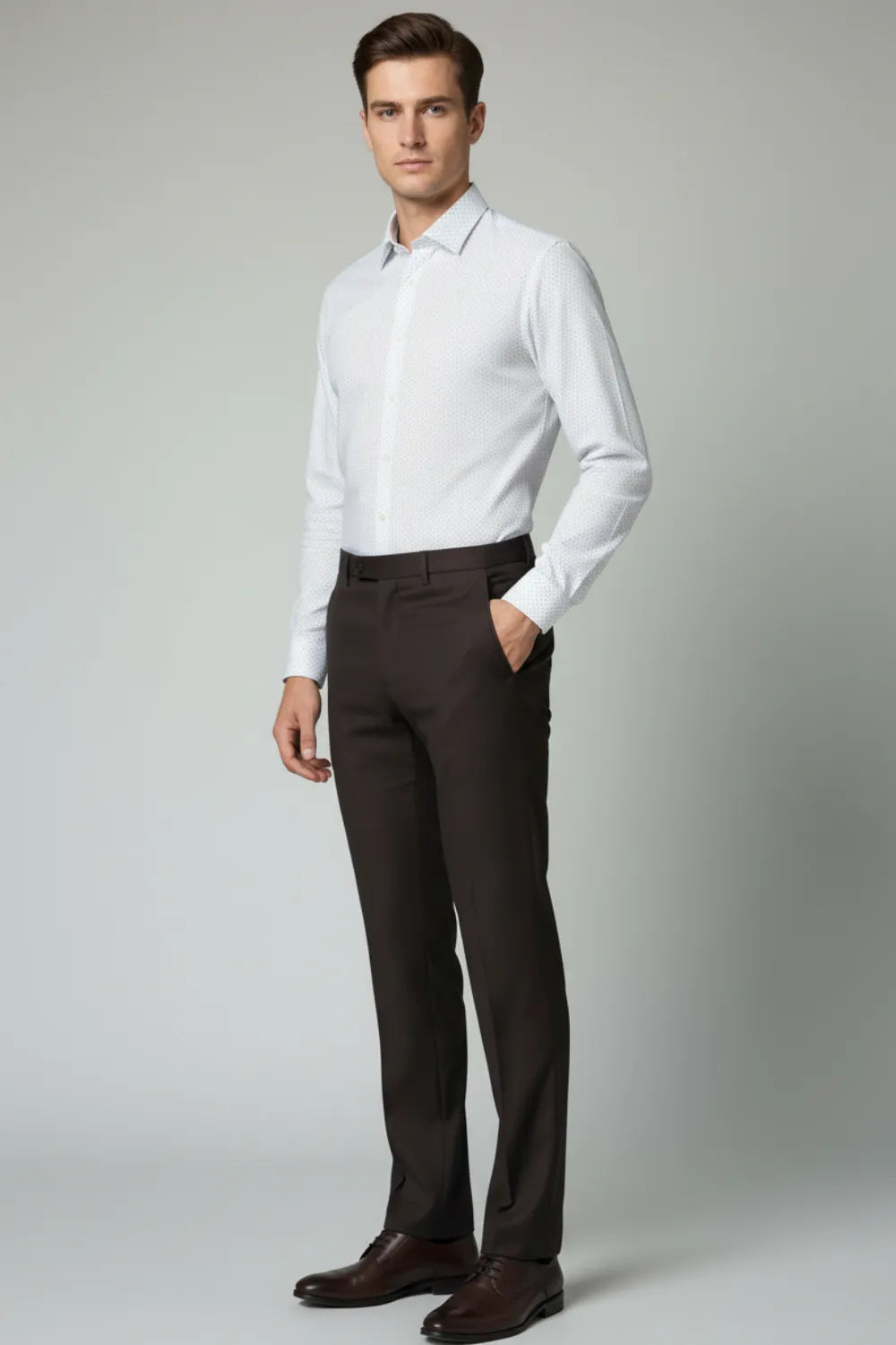 Man wearing a white dress shirt and dark brown pants against a gray background