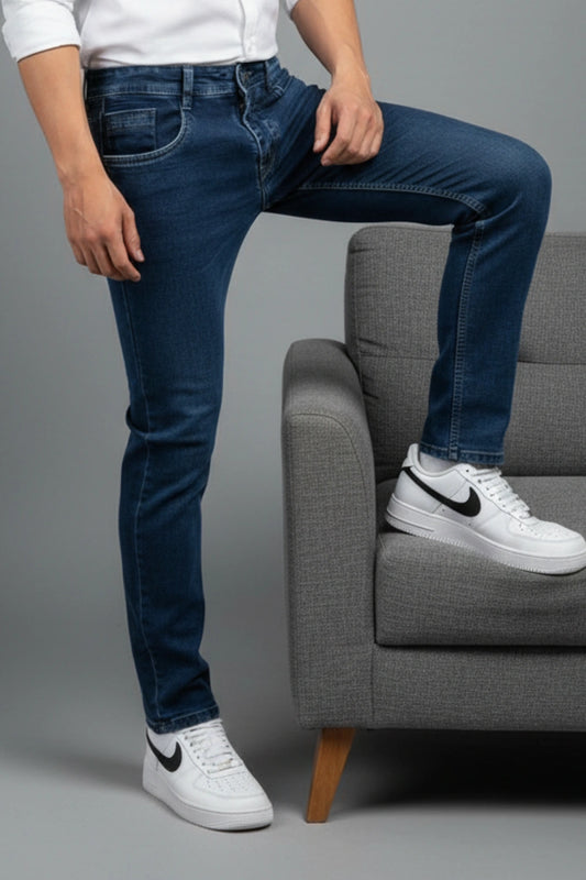 A man wearing light blue slim fit jeans and a white t-shirt sitting on a high stool, demonstrating a relaxed mid-rise fit.