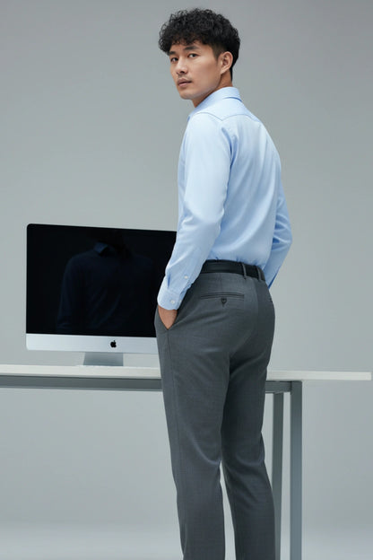 Man in a light blue shirt and gray pants standing in front of a computer monitor.