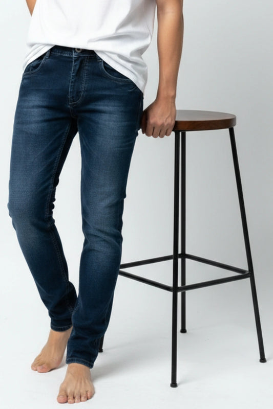 Person wearing slim fit blue jeans standing next to a wooden stool on a white background
