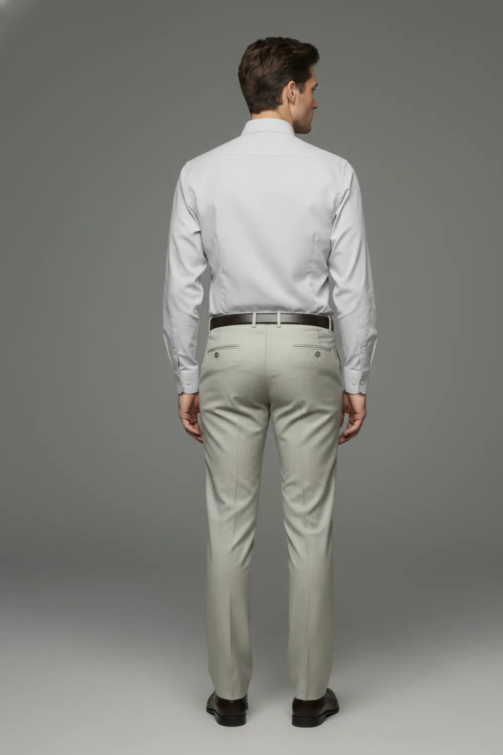 Man wearing a light gray shirt and formal pants against a gray background