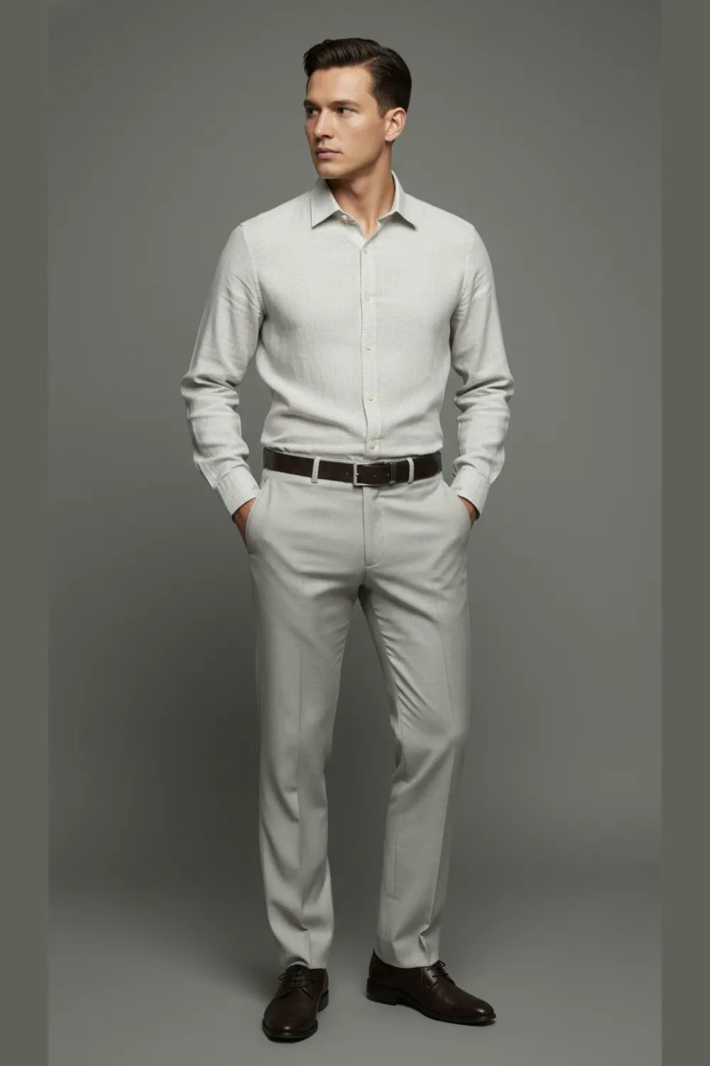 Man wearing a shirt and White  pants with a belt, standing against a gray background.